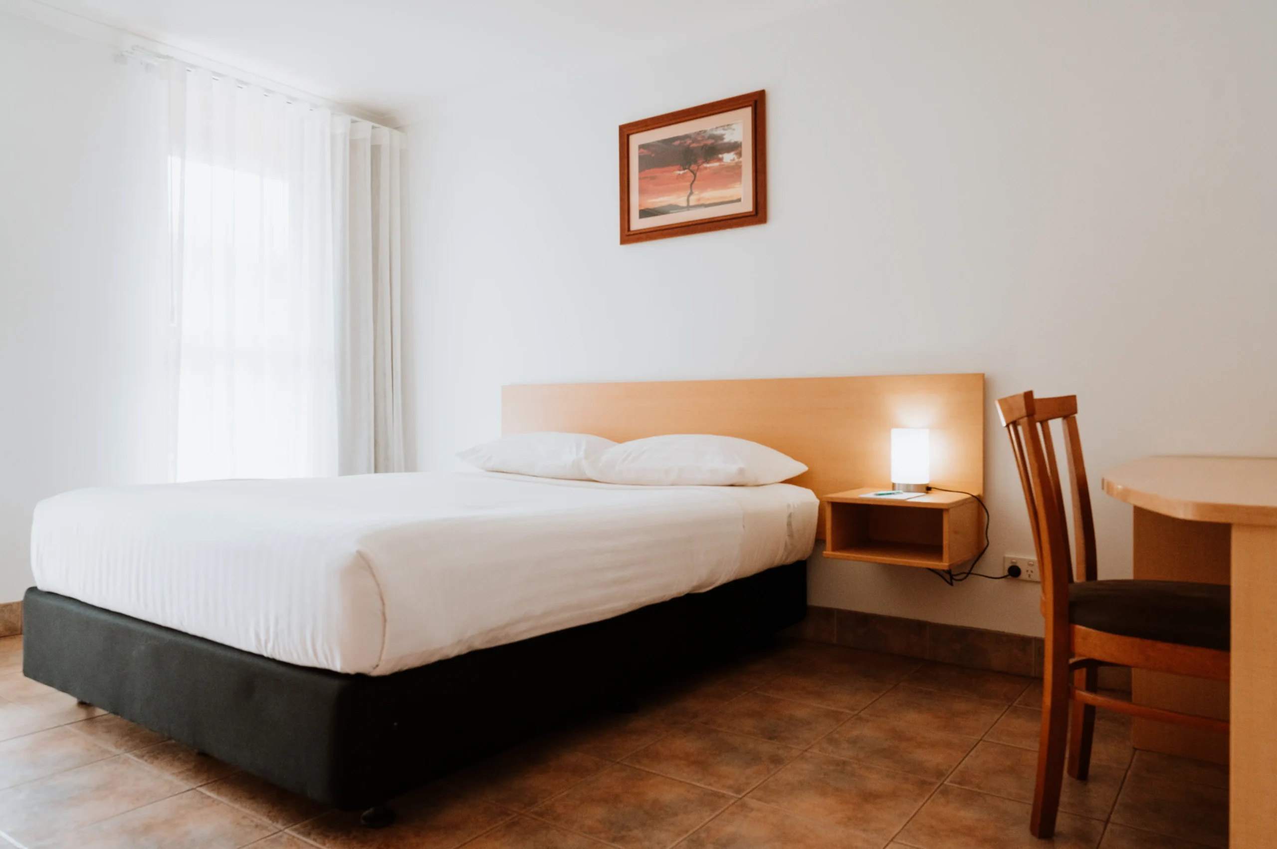 Image of a deluxe room showing the bed, a bright window and a desk with chair