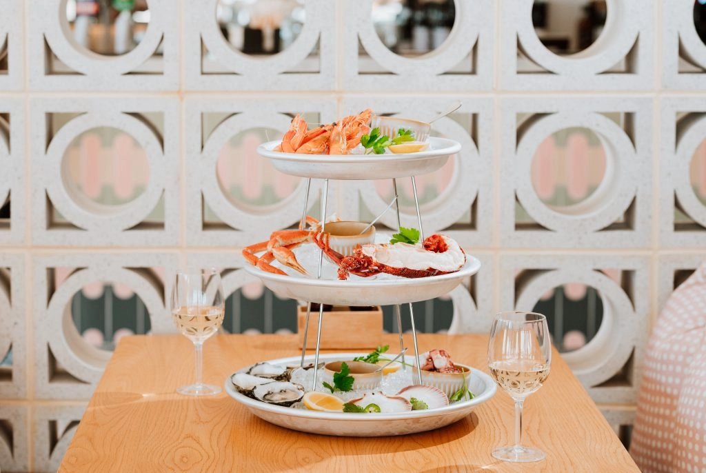 A seafood tower featuring shrimp, oysters and other shellfish paired with white wine